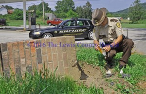 Deputy Bryon Walker gathers evidence at the entrance to Indian Hills after an auto struck and damaged one of the two brick columns there. - Photo by Dennis Brown